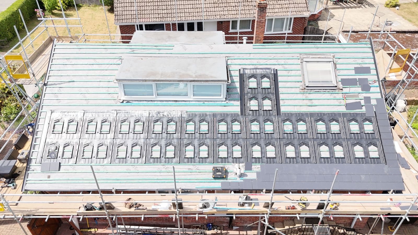Grey slates being laid up to in-roof solar trays on a Canterbury roof