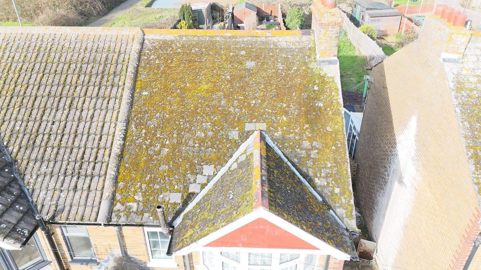 Moss-covered roof of a semi-detached house near Sittingbourne before re-roofing, front gable in view