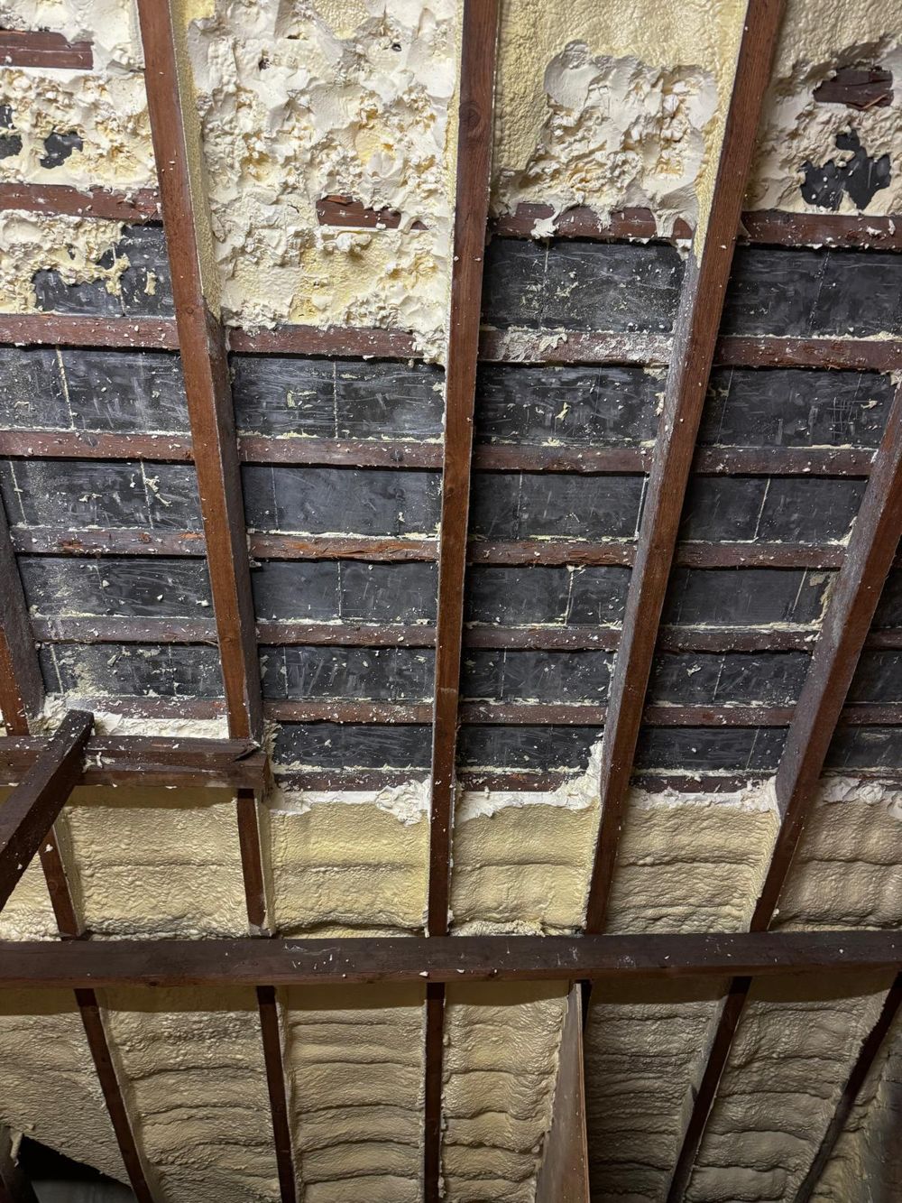 Spray foam partly scraped back to the old bitumen felt on the underside of a roof
