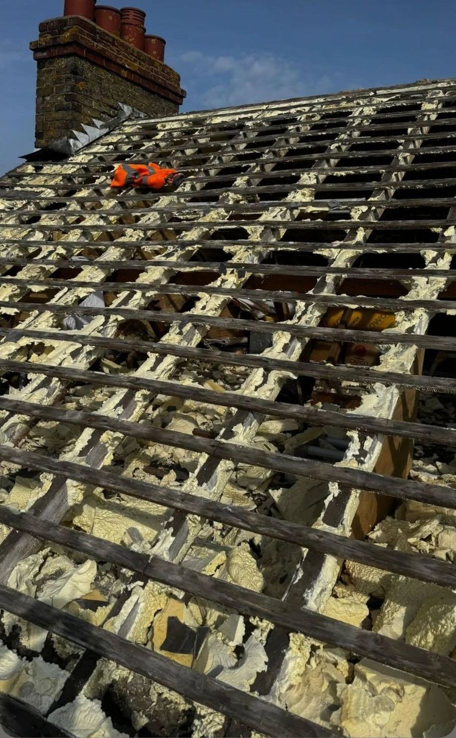 Roof stripped to the battens with spray foam visible between every rafter, chimney behind