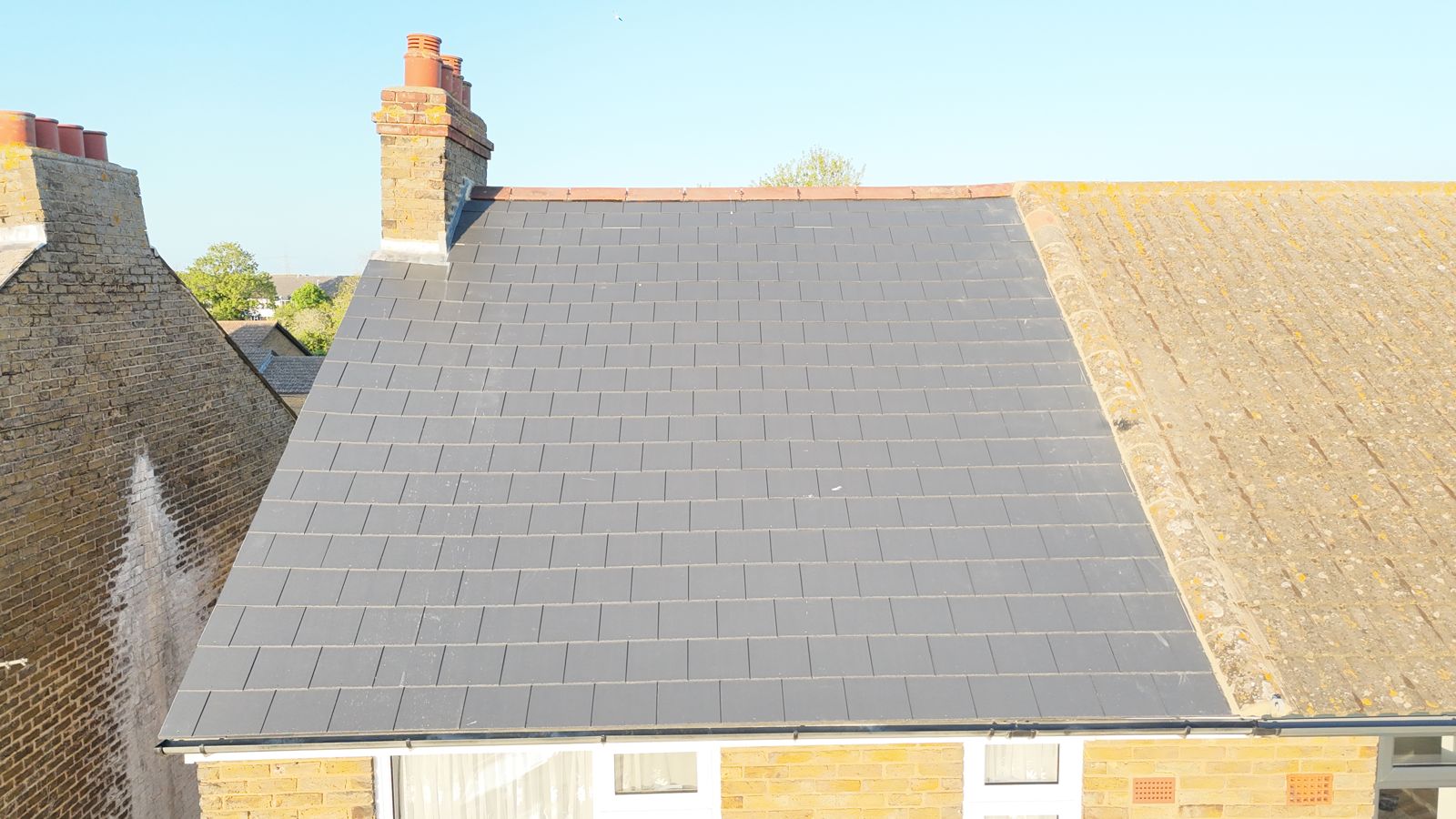 Close view of new slates laid up to the party wall line beside a neighbour's older tiled roof